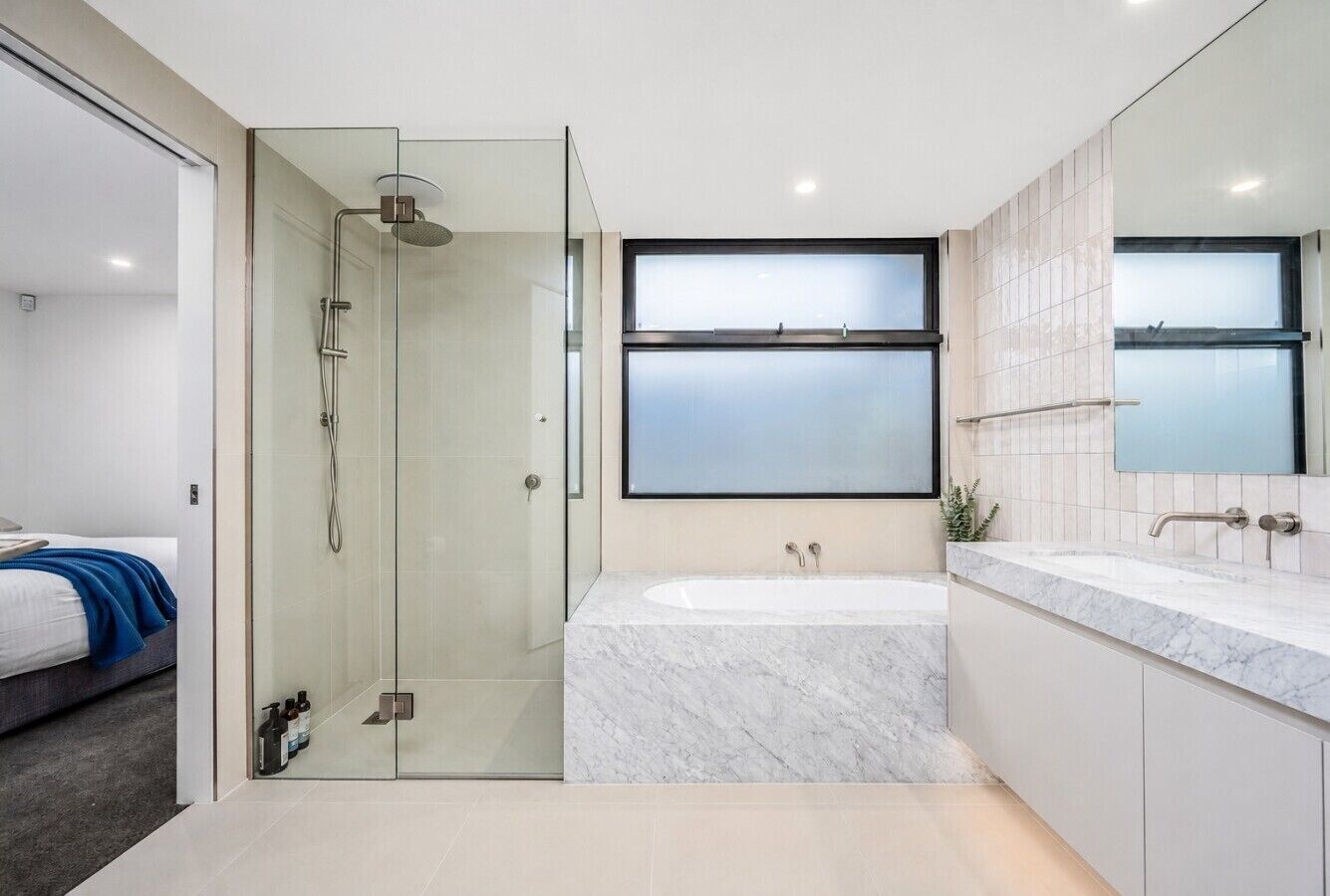A modern bathroom with a glass shower enclosure, a freestanding bathtub, and a large mirror above the sink.