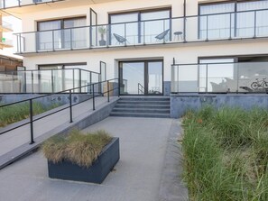Ein modernes Gebäude mit Glasfassade, einer Treppe zum Eingang und einem Pflanzbehälter mit Gras.