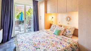 Une chambre à coucher avec une couvre-lit à motifs floraux, une table de chevet avec une lampe et une vue sur l’extérieur grâce à une porte coulissante.