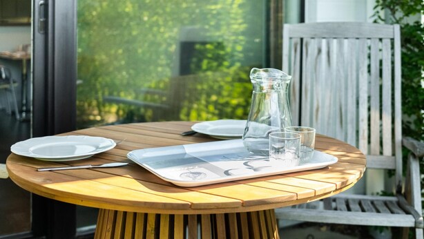 Une table ronde en bois, avec un plateau, des assiettes, des couverts et un pichet.