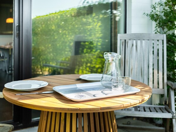 A round wooden table with a tray, plates, cutlery, and a pitcher. - Charming apartment close to the the beach (Sint-Idesbald)