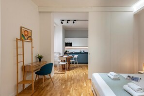 A compact room with a bed, a desk with a chair, a dining table with chairs, a kitchen area, and a painting on the wall. - Maison Columbus in the Heart of Genova (Genoa)