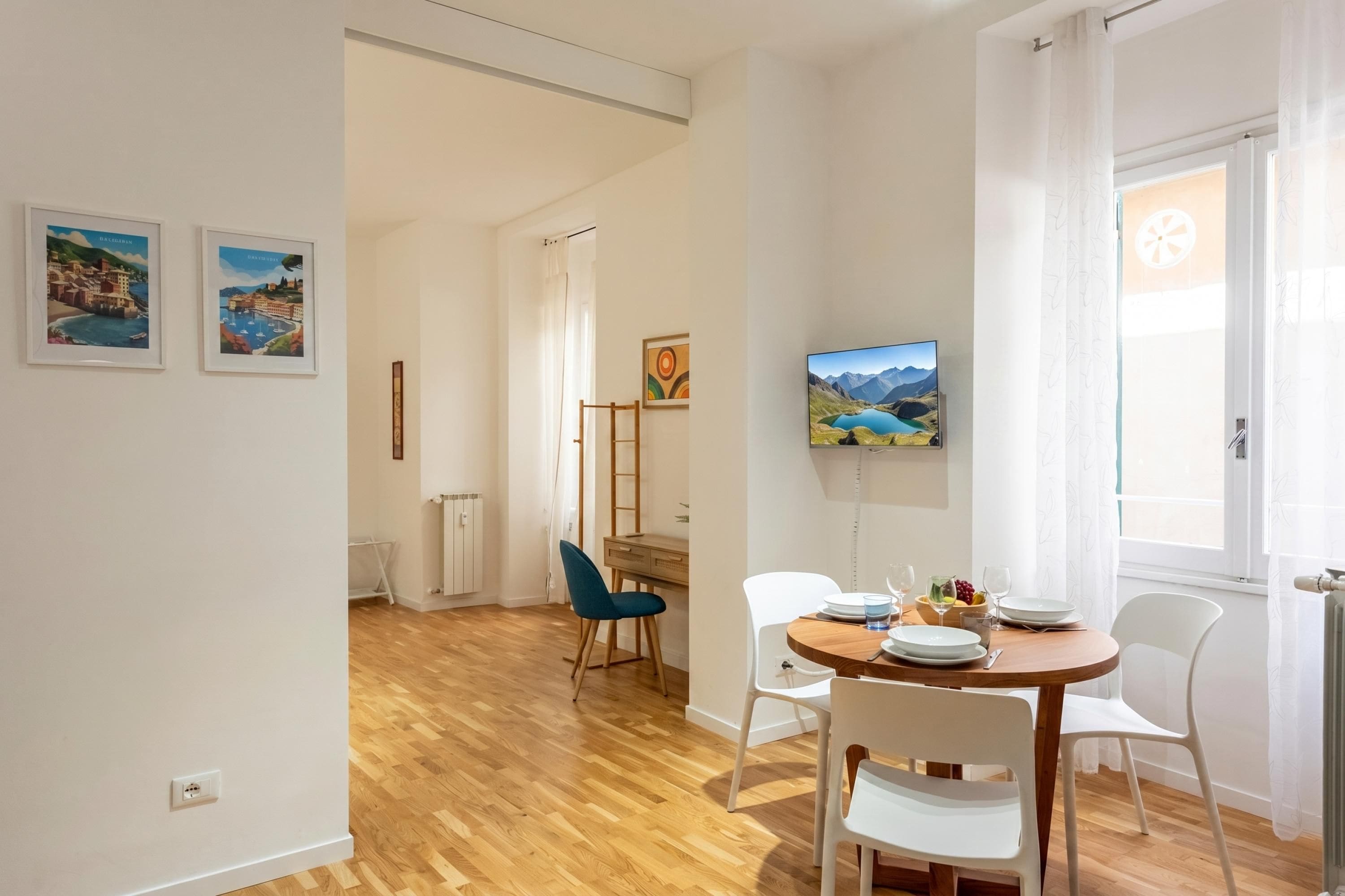 Un coin repas avec une table en bois, des chaises blanches et un téléviseur fixé au mur.