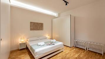 A bedroom with a bed, bedside lamps, a wardrobe, and a white shelf unit.