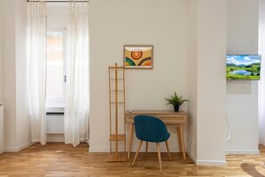 A room with a wooden desk, a blue chair, a ladder, a framed picture, and a TV on the wall.