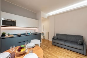 A modern kitchen with a built-in oven, a dining area with a wooden table and chairs, and a grey sofa in the living area. - Maison Columbus in the Heart of Genova (Genoa)
