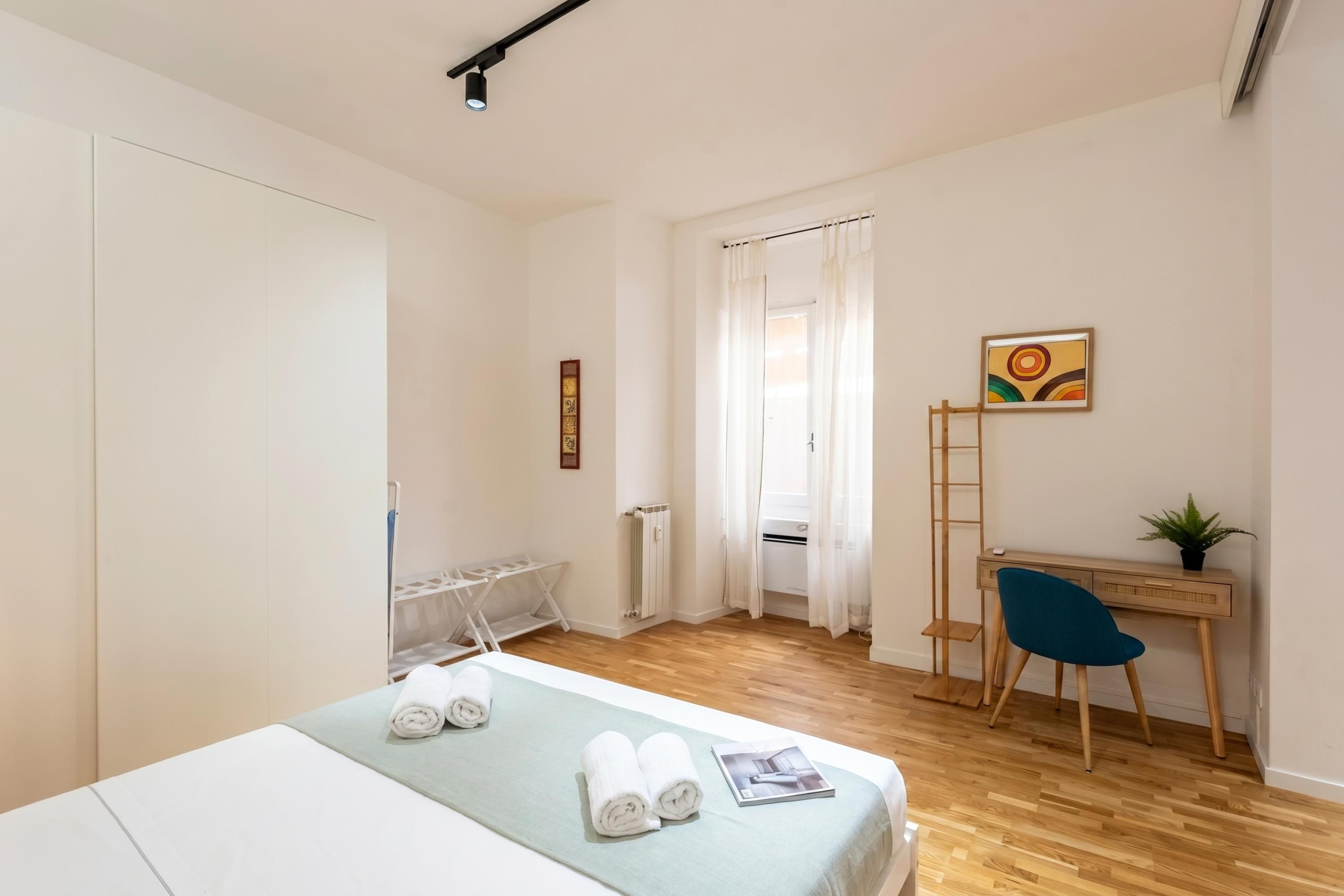 A bedroom with a bed, a desk, a chair, a radiator, and a window with curtains.