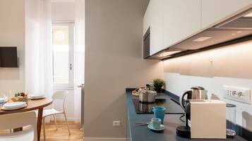 A modern kitchen with a dining area, a kettle, a coffee machine, and a window with curtains.
