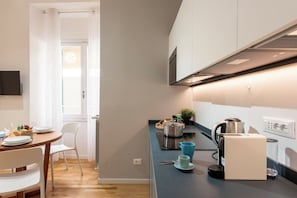 A modern kitchen with a dining area, a kettle, a coffee machine, and a window with curtains. - Maison Columbus in the Heart of Genova (Genoa)