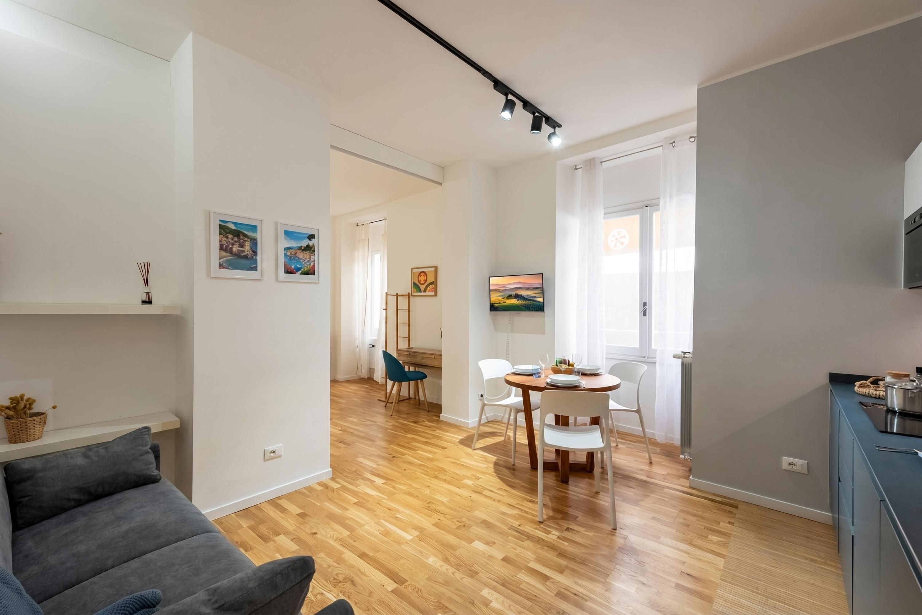 Uma sala moderna com sofá, mesa de jantar e cadeiras, área de cozinha com armários, e um corredor que dá para outro quarto.