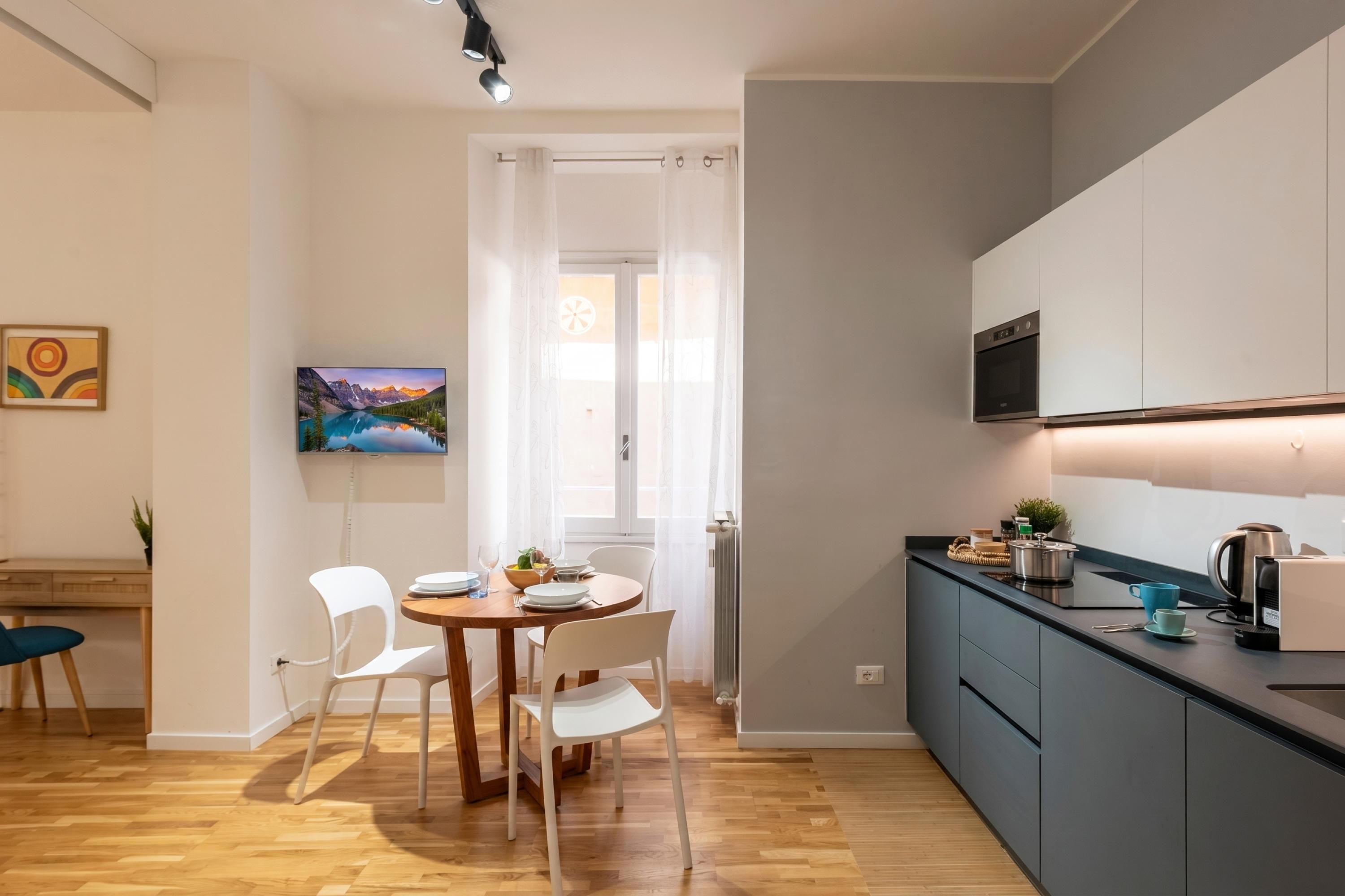 Una cocina moderna con horno empotrado, un comedor con mesa de madera y sillas blancas, y vistas a un paisaje montañoso a través de una ventana.