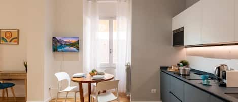 Una cocina moderna con horno empotrado, un comedor con mesa de madera y sillas blancas, y vistas a un paisaje montañoso a través de una ventana.