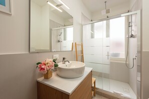 Casa de banho moderna com lavatório branco, espelho e cabine de duche em vidro.