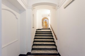 Una escalera con barandilla, paredes blancas y un ventanal decorativo en la parte superior.