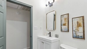 A bathroom with a toilet, a sink, and two mirrors. There are two framed artworks on the wall. - Charming, Cozy, Central & Convenient Home (Dallas)
