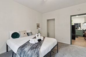 Een moderne hotelkamer met een bed, nachtkastje, wandlamp en een deur naar een keuken.