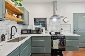 Een keuken met een spoelbak, een fornuis, een magnetron en een waterkoker.