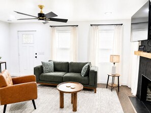 A living room with a sofa, armchair, round coffee table, ceiling fan, and a fireplace.
