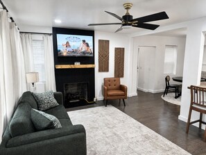 Un salon avec une cheminée, un téléviseur, un ventilateur de plafond et un coin repas.