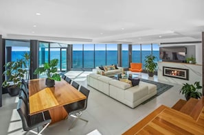 A modern living room with a large wooden table, a white sofa, and a fireplace.