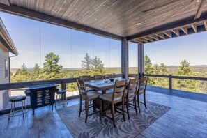 A covered outdoor dining area with a table and chairs, a bar stool, and a view of the landscape.