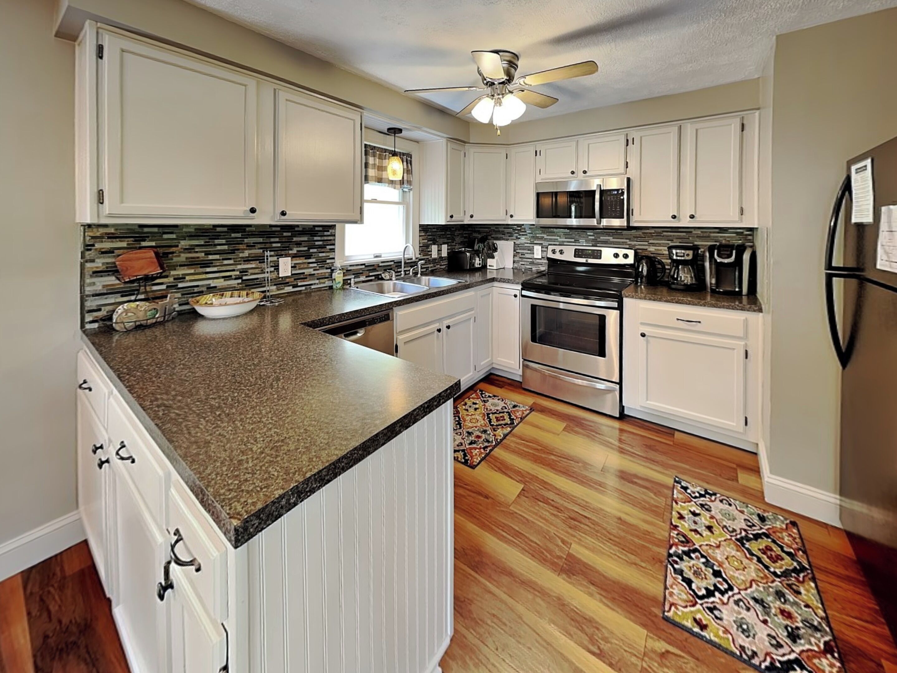 A kitchen with white cabinets, a granite countertop, a stove, a microwave, and a refrigerator.