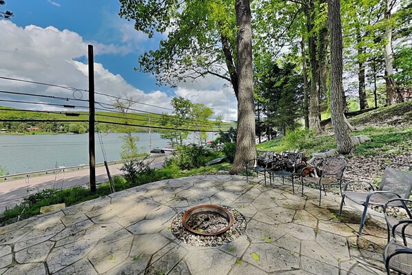 Un patio de piedra con un brasero, mobiliario exterior y vistas a un lago.