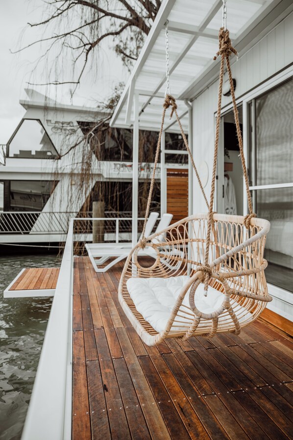 A wooden deck with a white outdoor seating area, including a wicker swing chair and a cushioned bench.