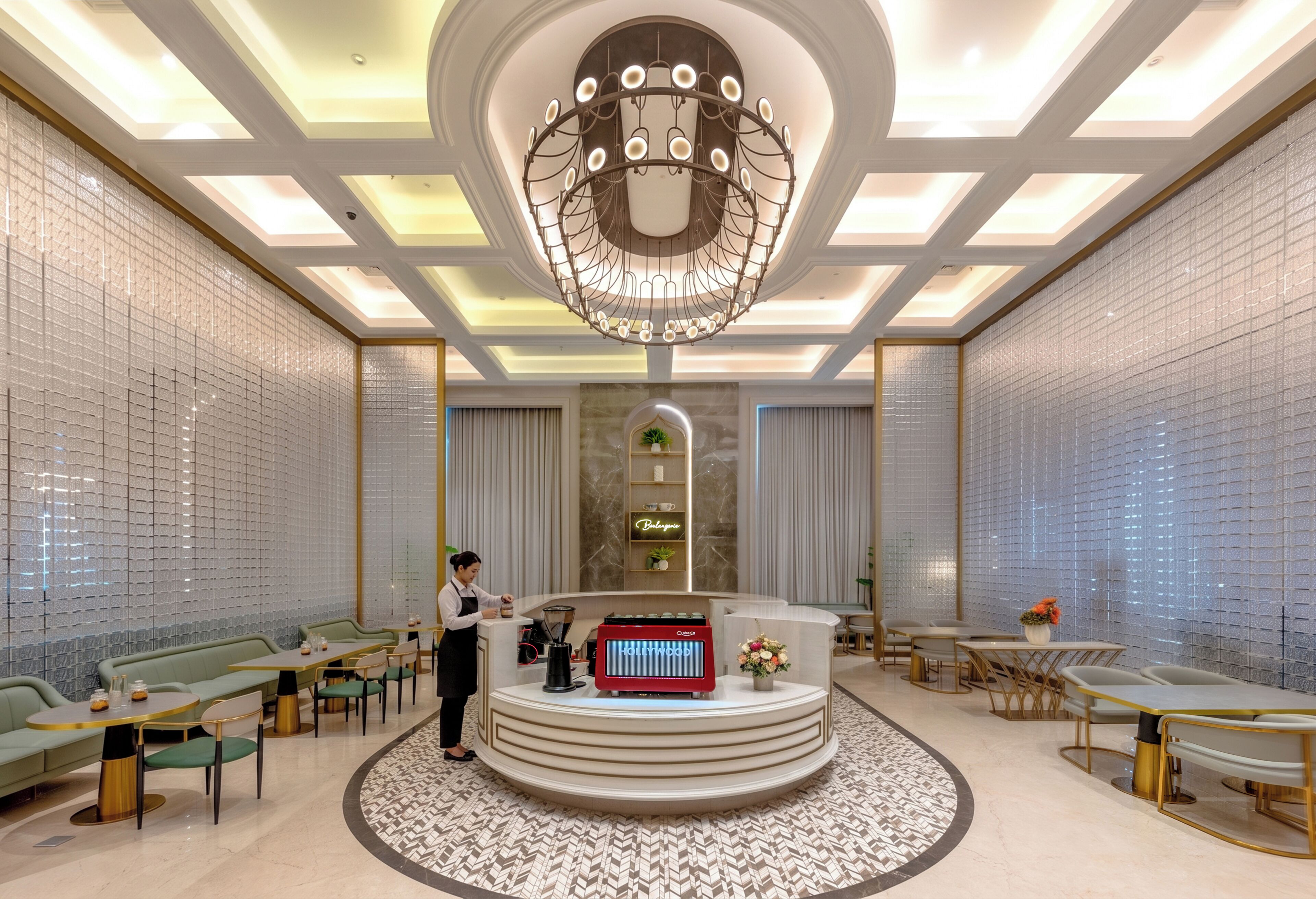 Vestíbulo de hotel con una recepción central, zonas de estar e iluminación decorativa en el techo.