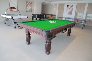 Una mesa de billar con superficie de fieltro verde, una vara de billar y una bola blanca.