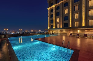 Piscina en la azotea con vistas a la ciudad, zona de bar y edificio de arquitectura clásica.