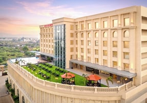 Un hotel con una amplia fachada de vidrio, varios balcones y una terraza ajardinada.
