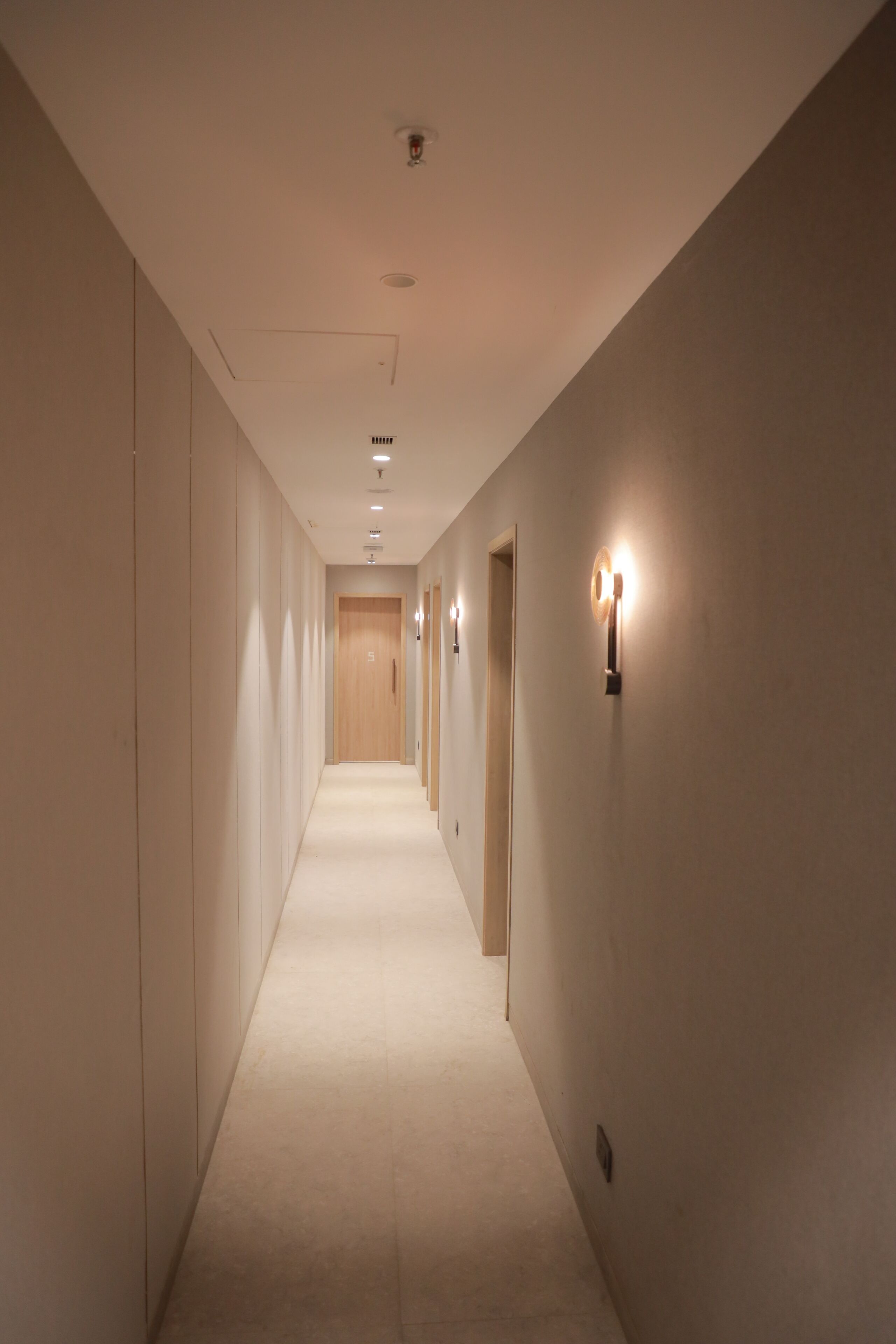 Un pasillo largo y estrecho con piso alfombrado, iluminación empotrada y lámparas fijadas a la pared.