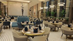 Een ruim restaurant met ronde tafels, stoelen en een centraal zitgedeelte met een blauwe bank.