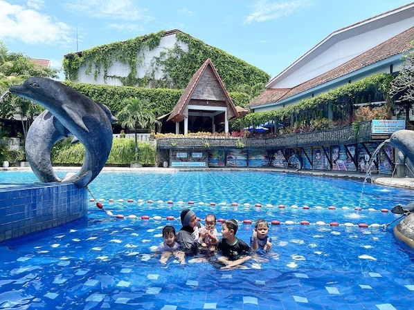 Une piscine ornĂ©e dâune sculpture de dauphin, un bĂątiment de style traditionnel et une allĂ©e couverte.