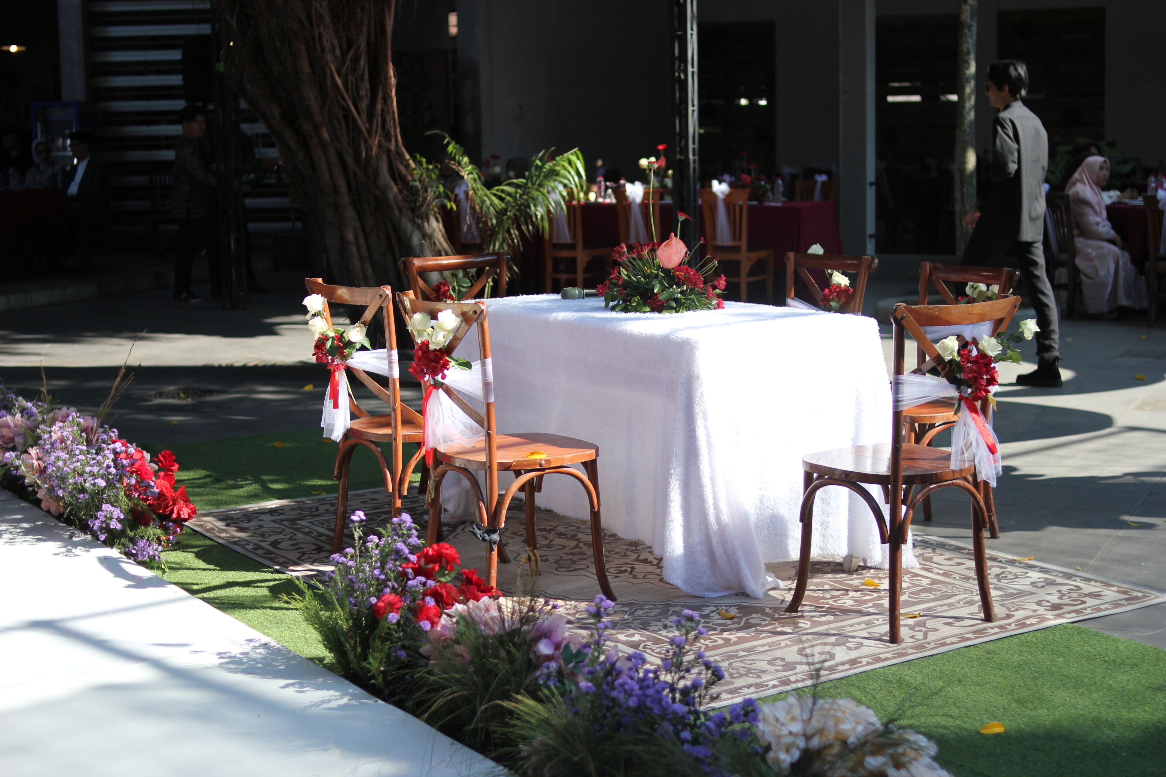 Un área de comedor al aire libre con una mesa redonda cubierta con un mantel blanco, rodeada de sillas de madera.