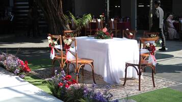 Un área de comedor al aire libre con una mesa redonda cubierta con un mantel blanco, rodeada de sillas de madera.