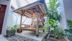 Un espace extérieur abrité, doté d’un toit de chaume, entouré de plantes et d’un mur de pierre.