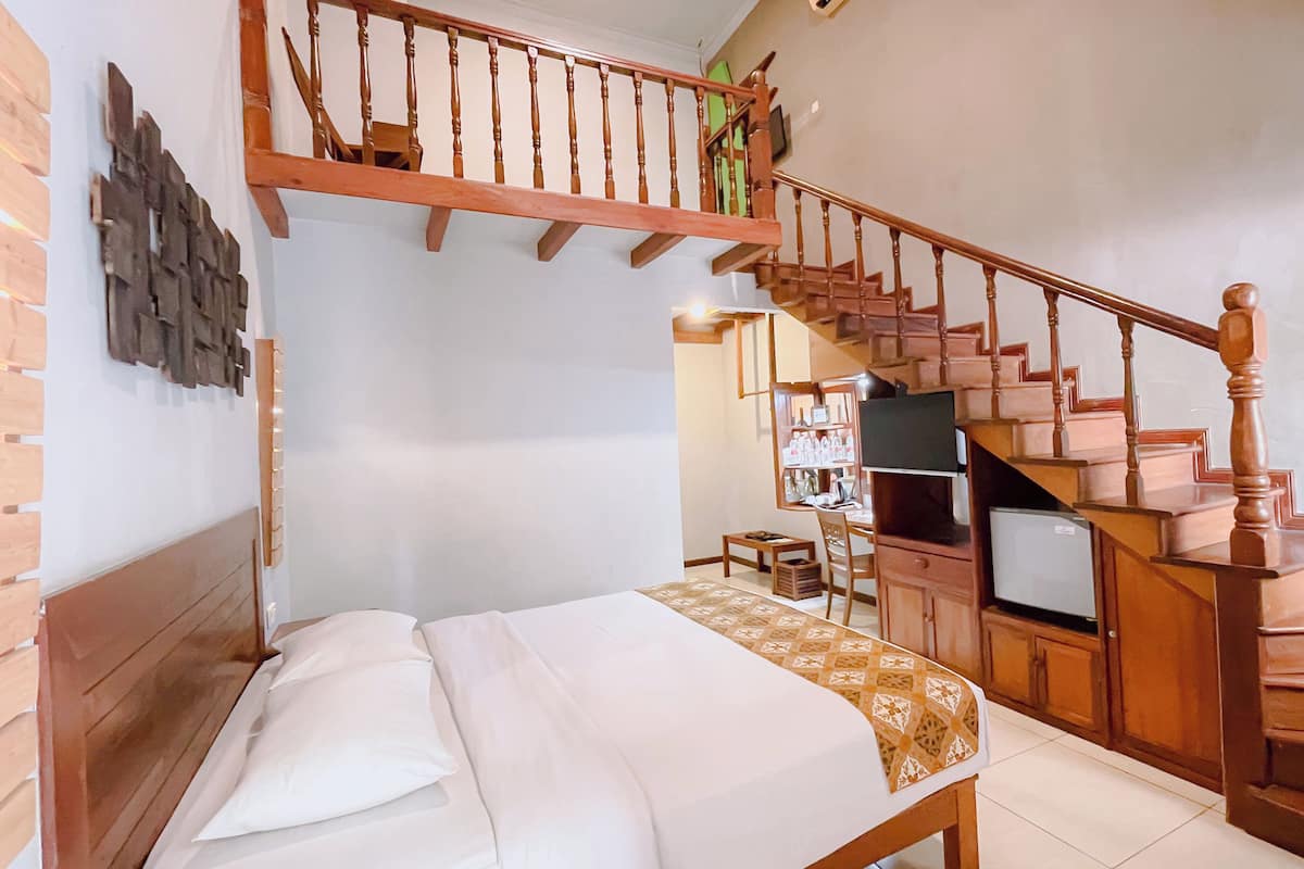 A bedroom with a bed, a wooden staircase, and a television in the background.