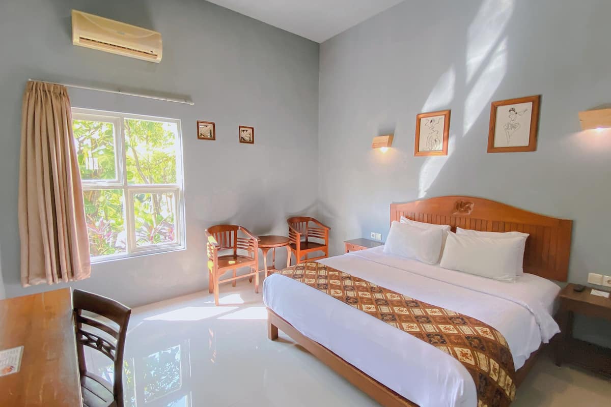 A bedroom with a bed, bedside table, chair, desk, and window.