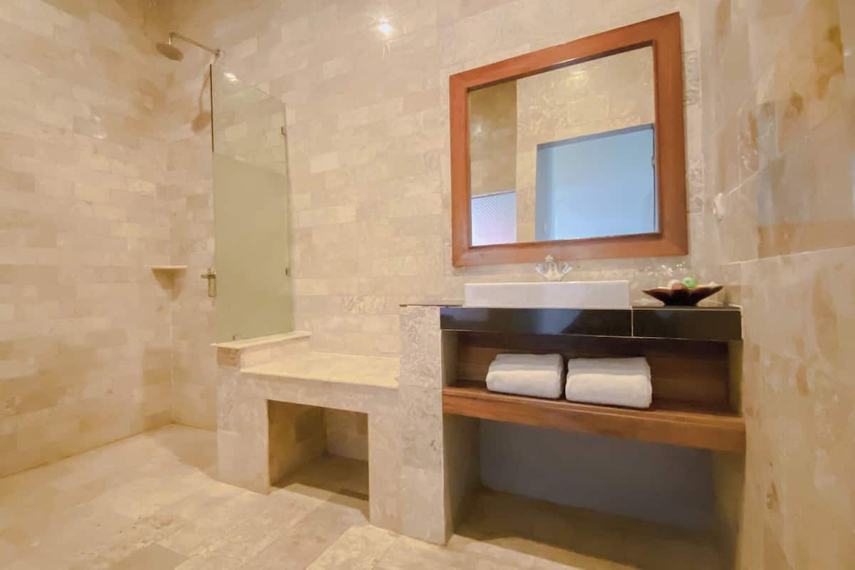 A bathroom with a shower, a sink with a mirror, and a shelf with towels.