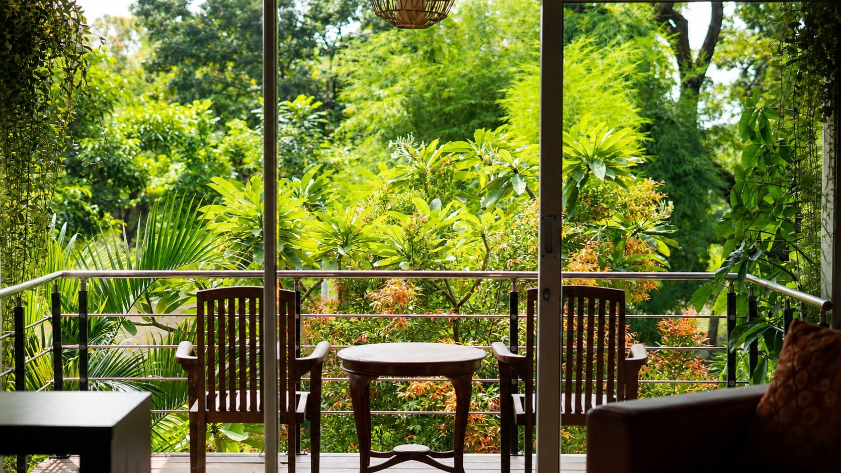 Een terras met een tafel en stoelen, omgeven door weelderig groen en een metalen hekwerk.
