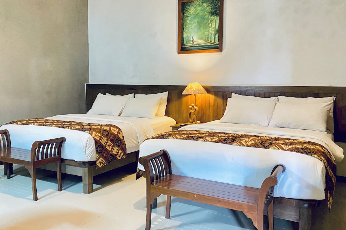 A hotel room with two beds, wooden chairs, a nightstand with a lamp, and a painting on the wall.