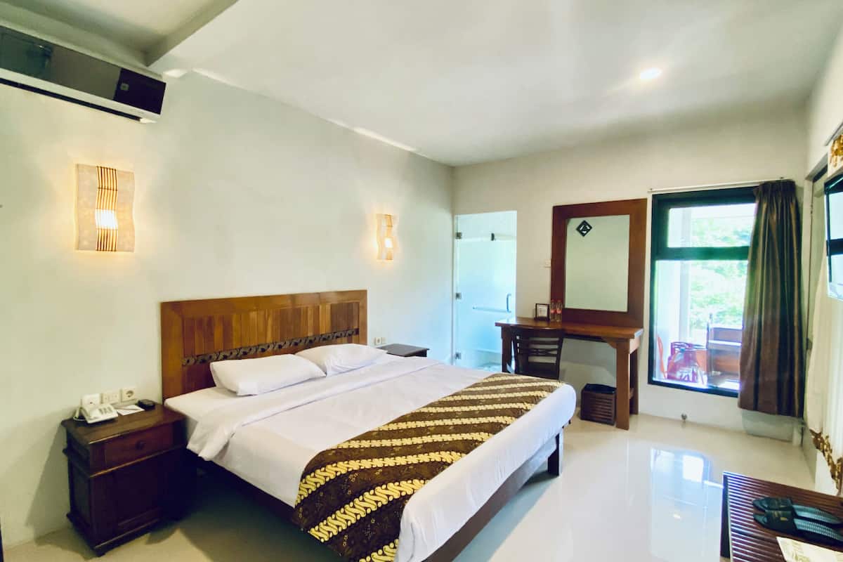 A hotel room with a large bed, bedside tables, a vanity, a mirror, and a window with curtains.