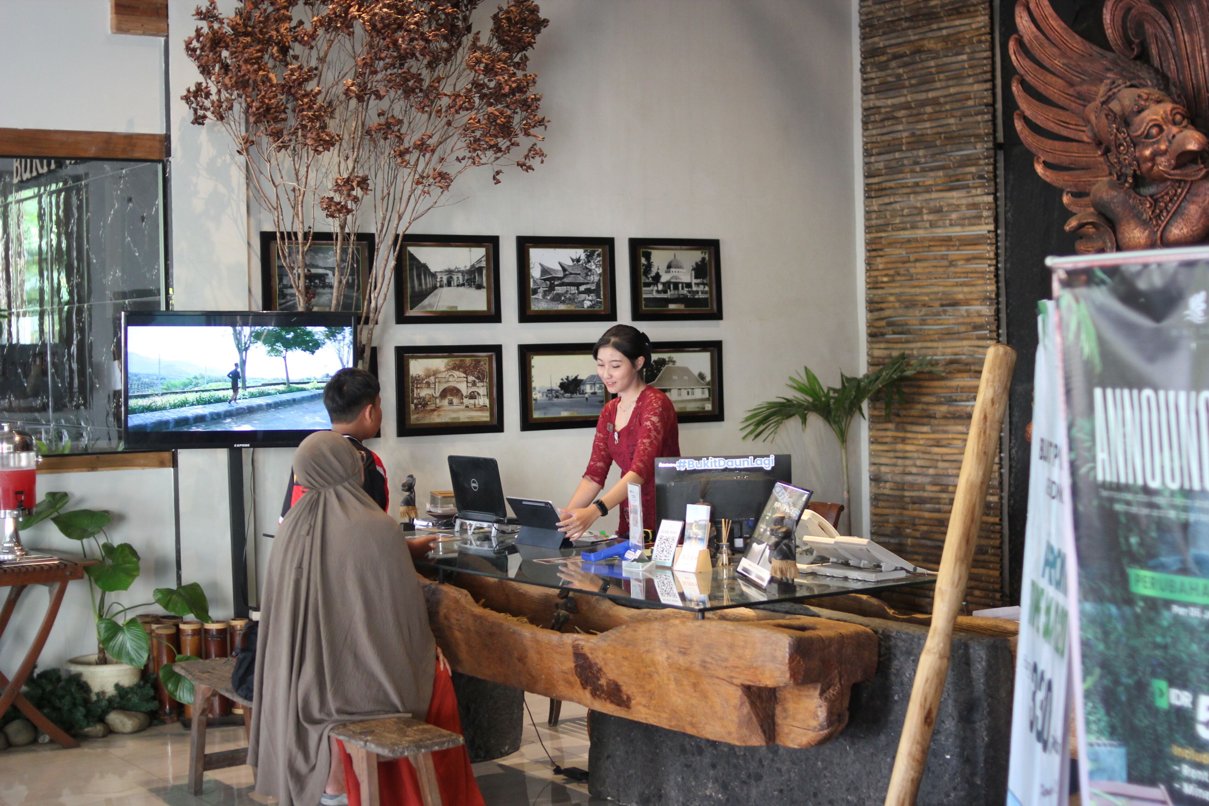 A reception area with a wooden counter, a television, framed pictures on the wall, and a decorative plant.