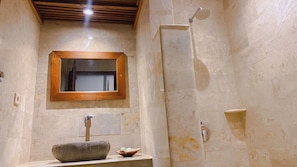 A bathroom with a stone sink, a wooden-framed mirror, and a shower.
