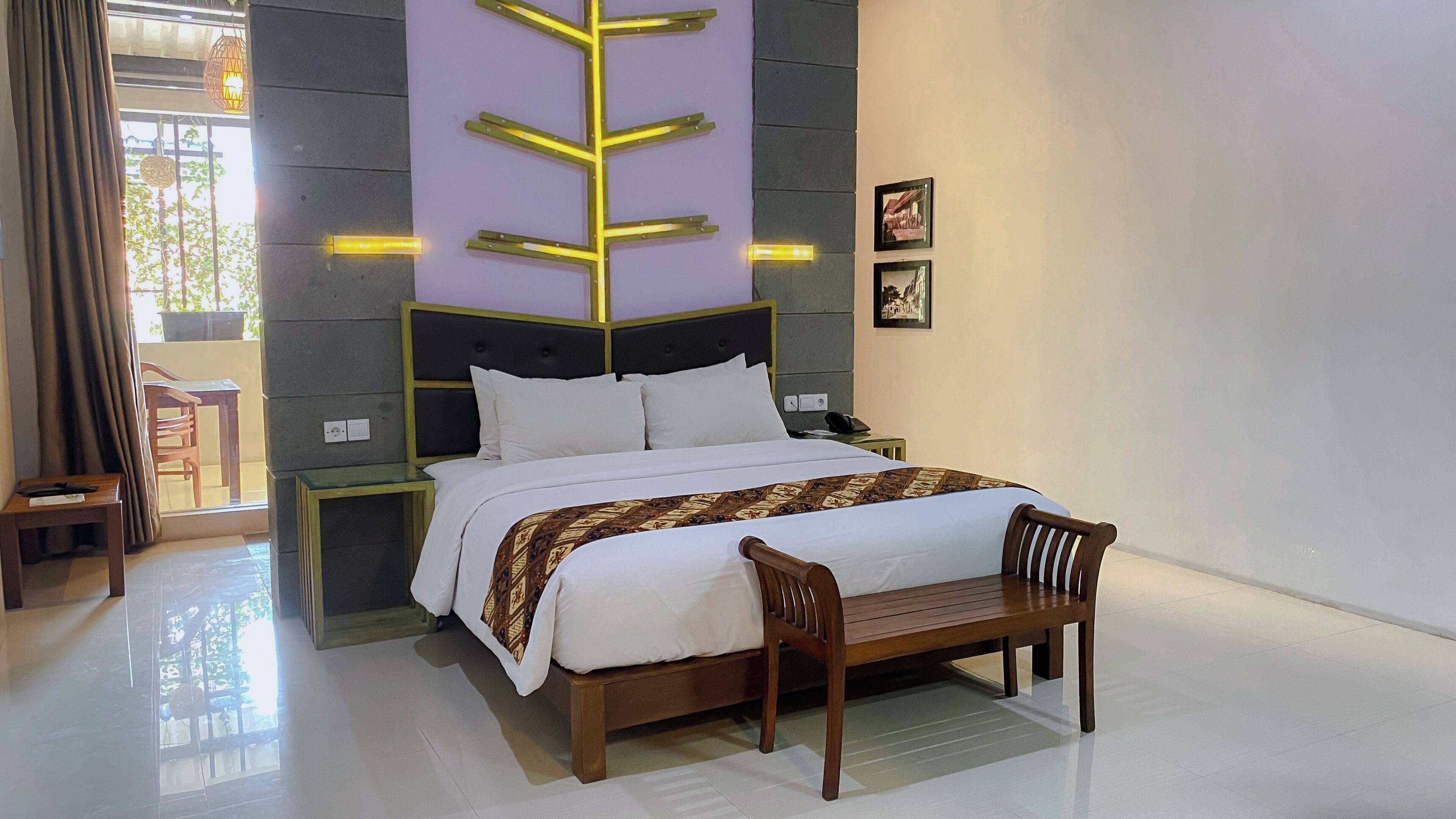 A modern hotel room with a bed, bedside tables, a bench, and a view of the outdoors.