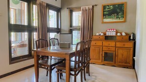 Un coin repas avec une table et des chaises en bois, un réfrigérateur, un meuble contenant des ustensiles de cuisine et un tableau accroché au mur.