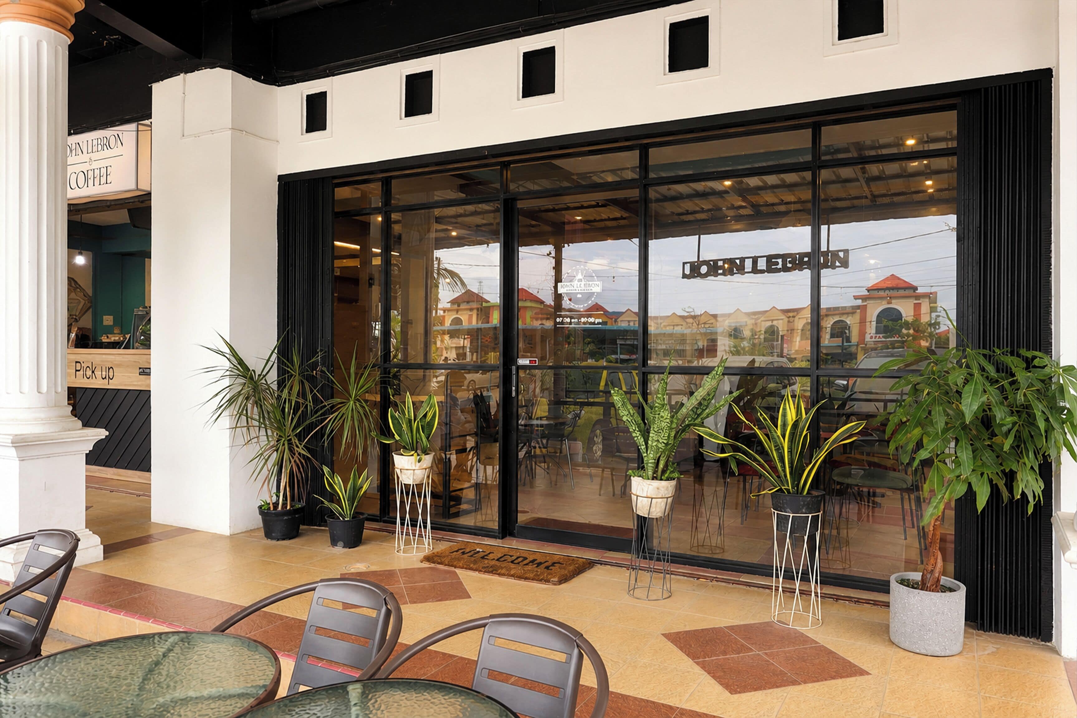 A hotel entrance with a glass facade, outdoor seating area, and potted plants.