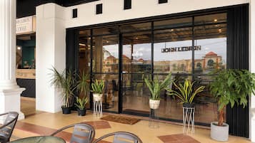 A hotel entrance with a glass facade, outdoor seating area, and potted plants.